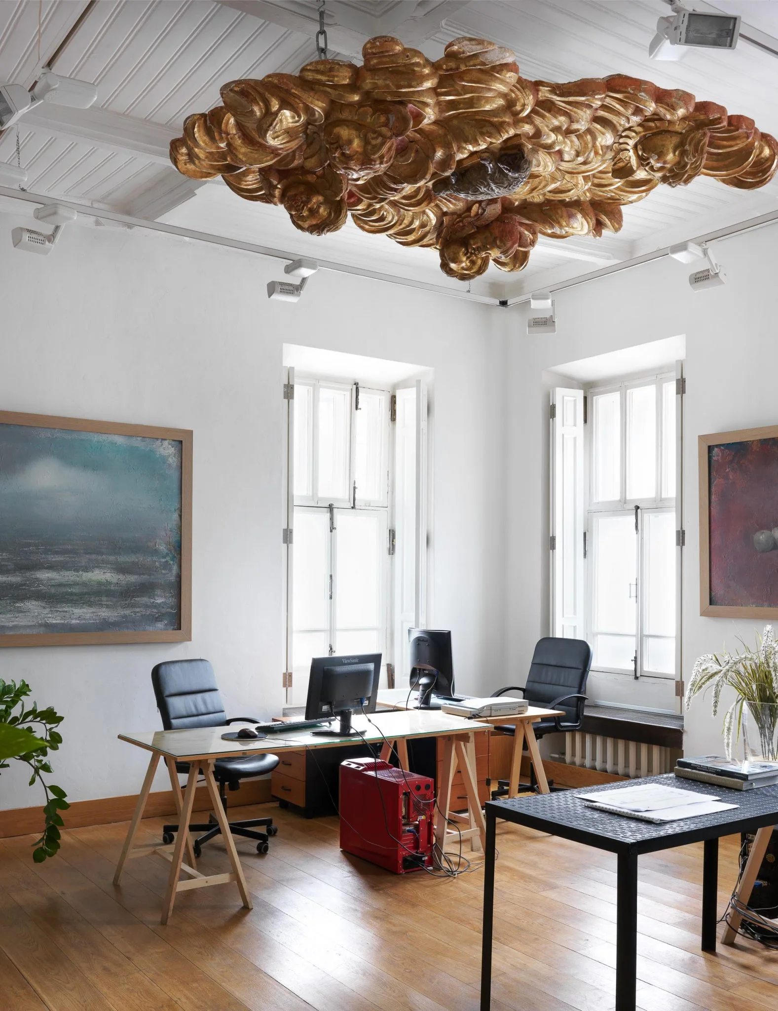 Espacio de trabajo luminoso en Moscú con arte, mobiliario diverso y una instalación dorada en el techo.