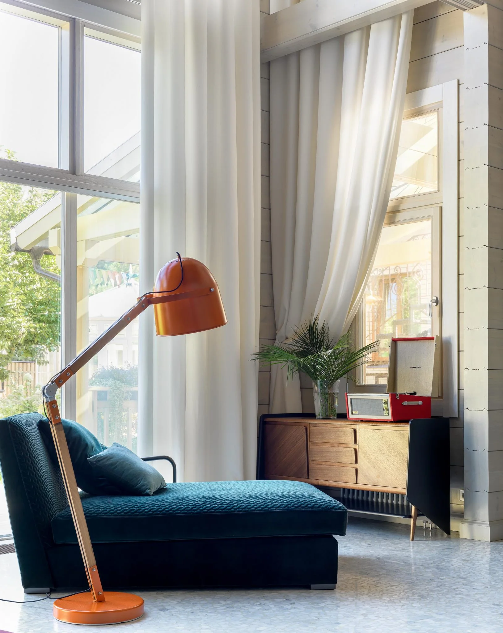 Rincón de lectura en una casa de Moscú con chaise longue oscura, lámpara naranja y tocadiscos.