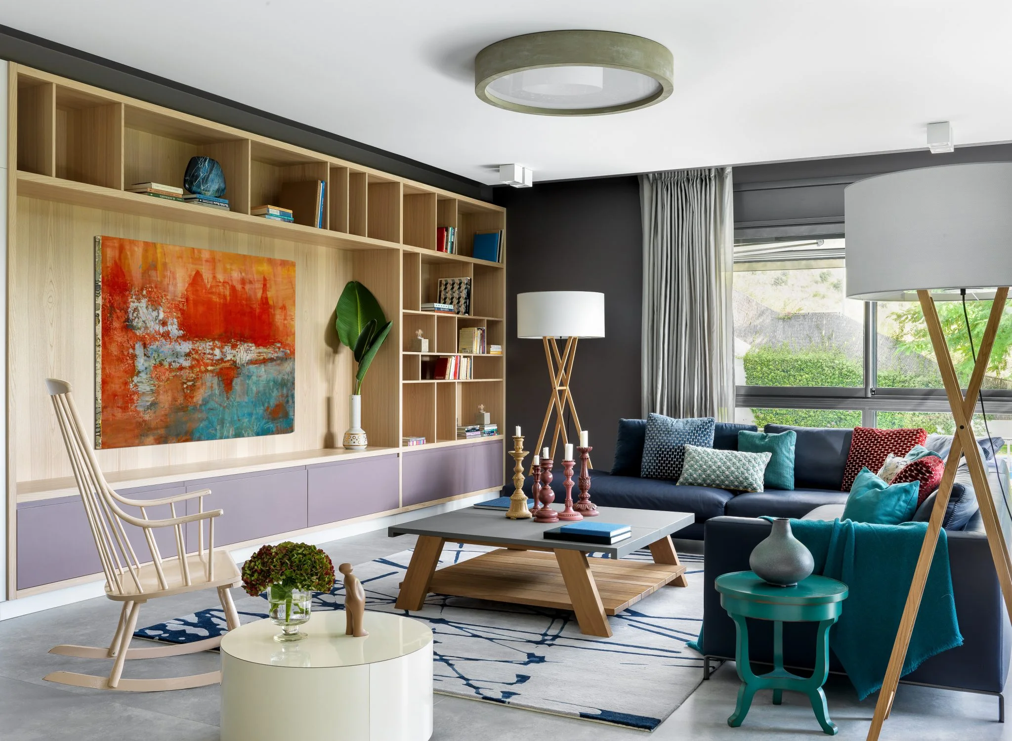 Vista amplia de una residencia privada en Barcelona con una pintura abstracta naranja y azul, una biblioteca de madera y un sofá en L
